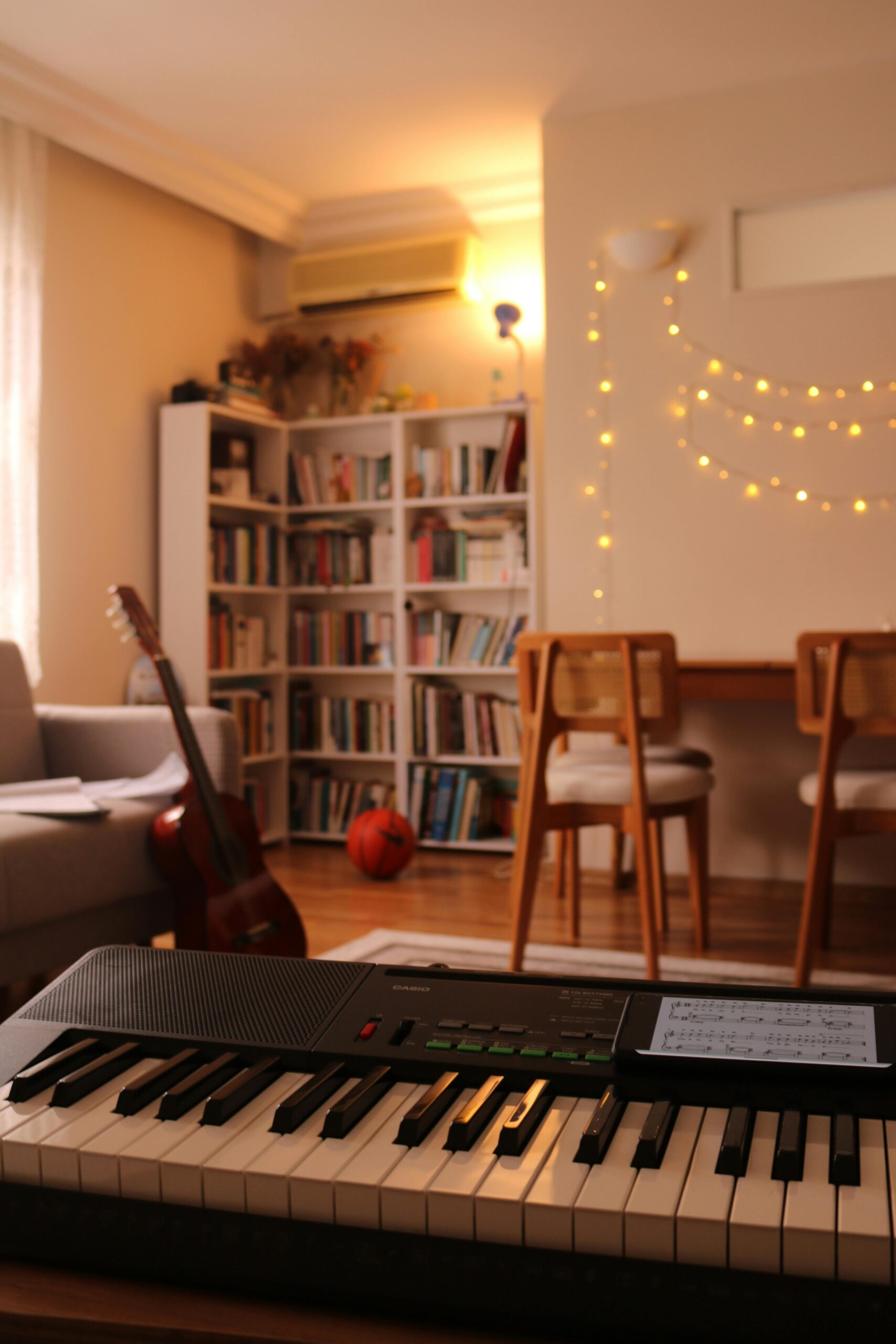 Warm and inviting living room with musical keyboard, bookshelf, and string lights.